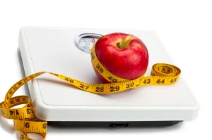 Tools for measuring weight and progress, including a scale, a tape measure, and an apple