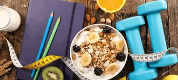 A composition of items for a diet plan, including a notebook, a tape measure, a dumbbell, and a bowl of healthy food with a lemon